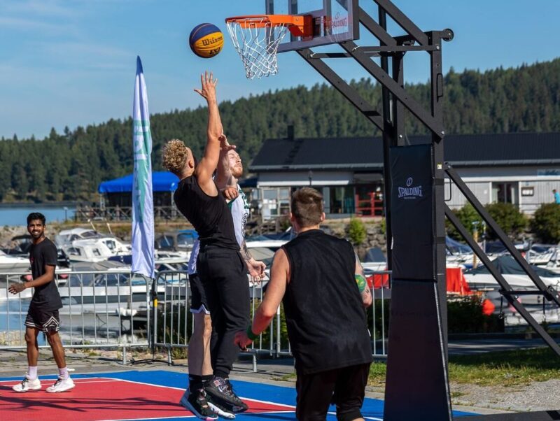 Energetic basketball game on a lakeside court with young men jumping and playing.