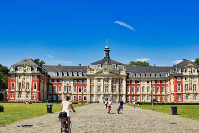 People bike in front of a large, ornate building
